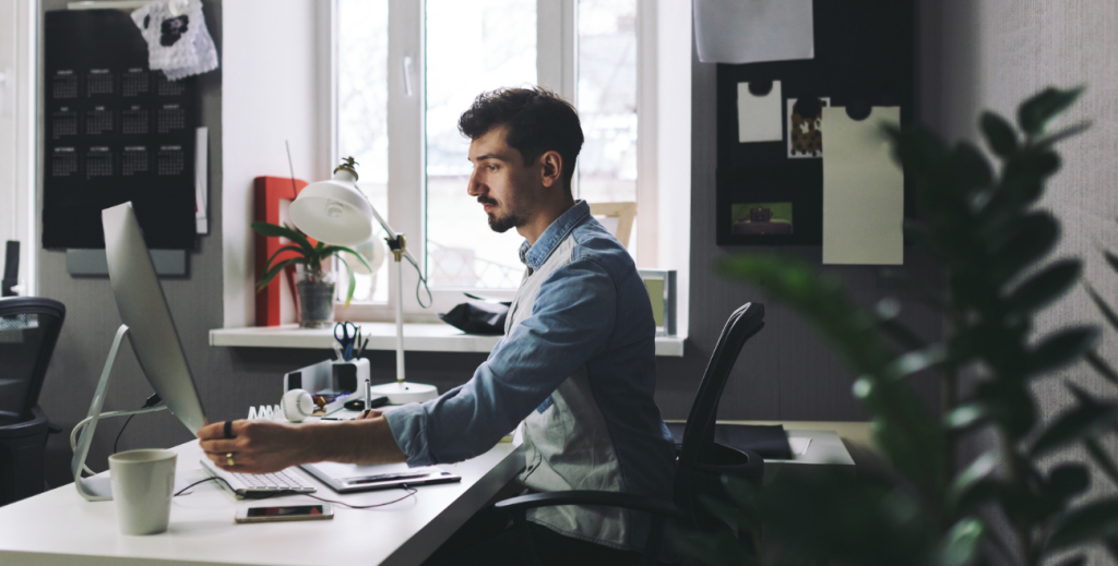 Colaborador trabalhando com computador e celular em escritório, ilustrando MDM e LGPD na segurança e gerenciamento de dispositivos móveis nas empresas.