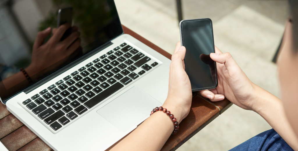 Pessoa utilizando smartphone ao lado de notebook, representando o BYOD nas empresas.