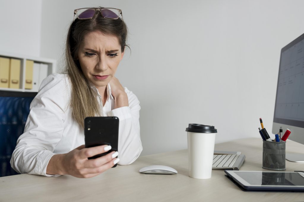 Mulher preocupada ao usar o celular no trabalho durante o expediente.