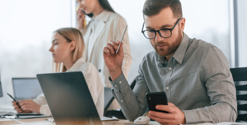 Profissionais utilizando dispositivos corporativos em ambiente de trabalho, representando o modelo CYOD (Choose Your Own Device) para uso de celulares e computadores na empresa.