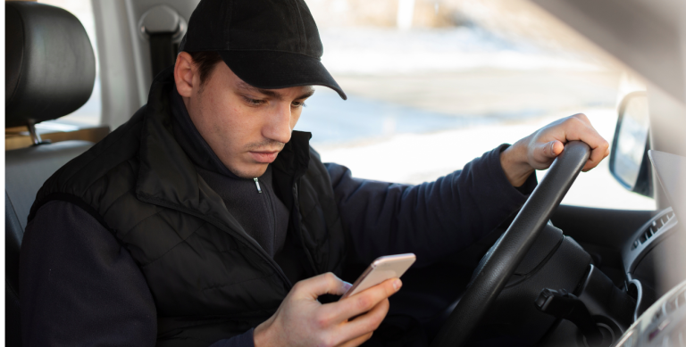 Motorista utilizando celular ao volante, ilustrando o bloqueio de tela por velocidade para aumentar a segurança com MDM